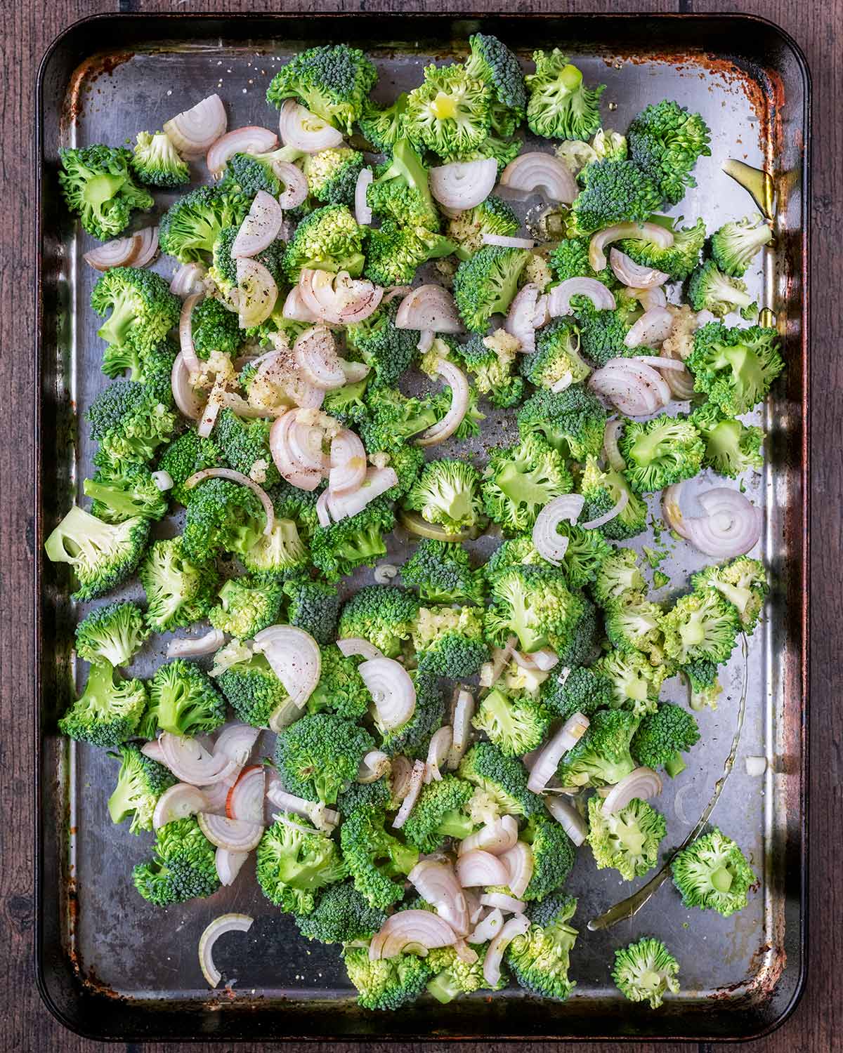 A large sheet pan with small broccoli florets and sliced shallots on it.