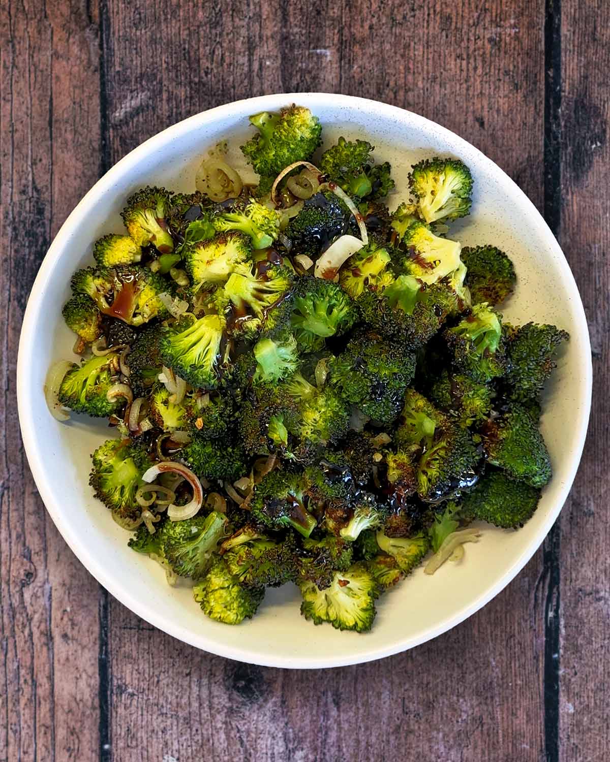 Cooked broccoli florets in a bowl with a dark sauce poured over them.