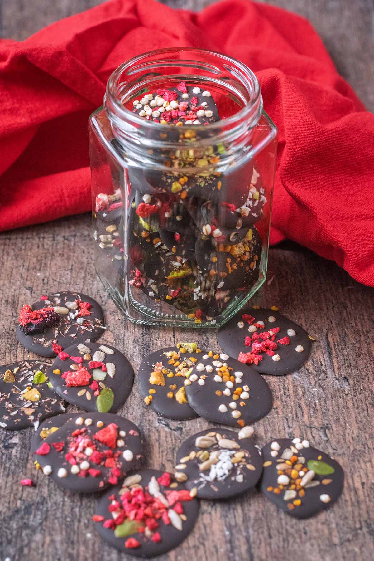 Homemade chocolate buttons on a wooden surface next to a jar full of more buttons.