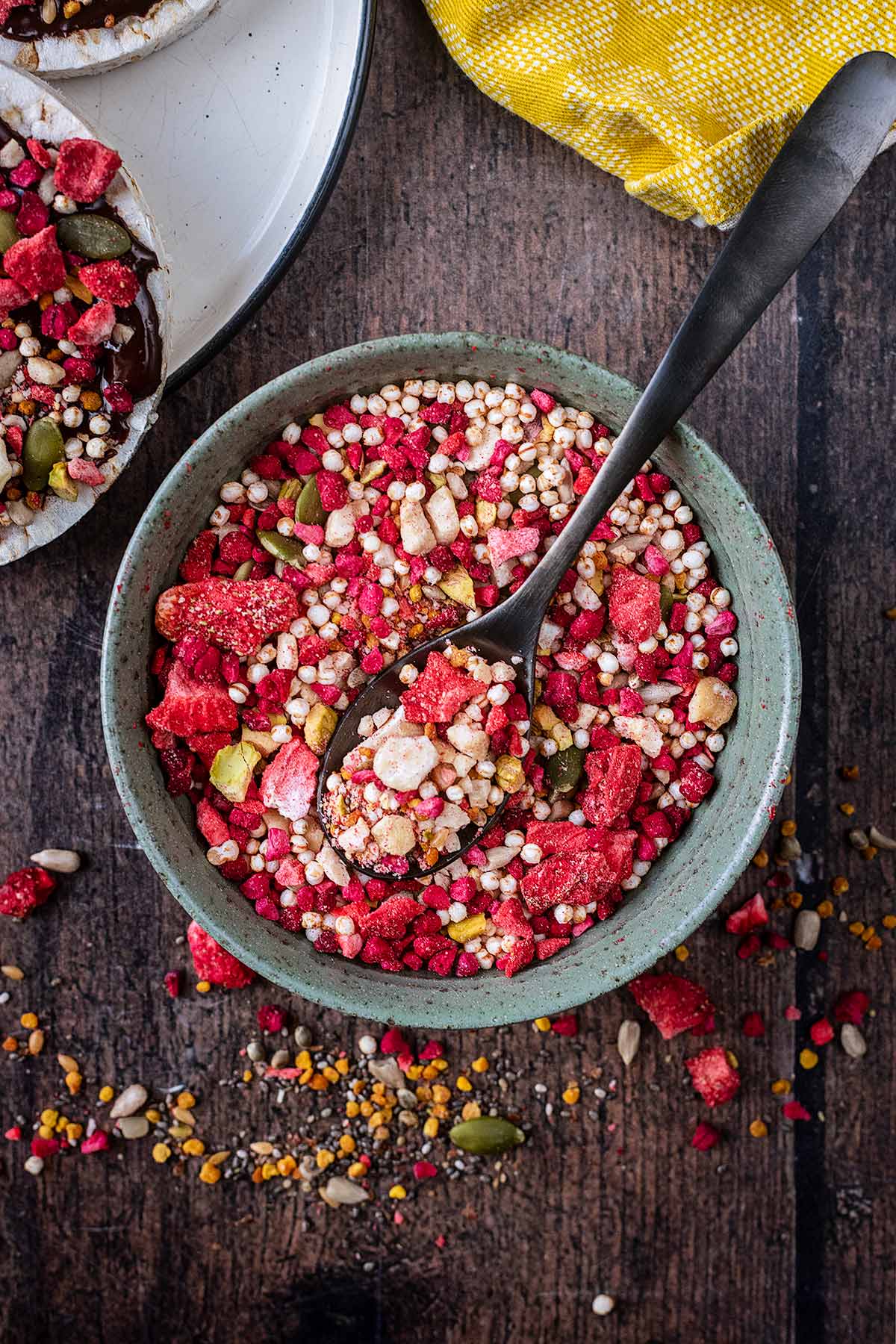 A bowl of mixed berries, nuts and seeds with some spilled on to the wooden surface beneath.