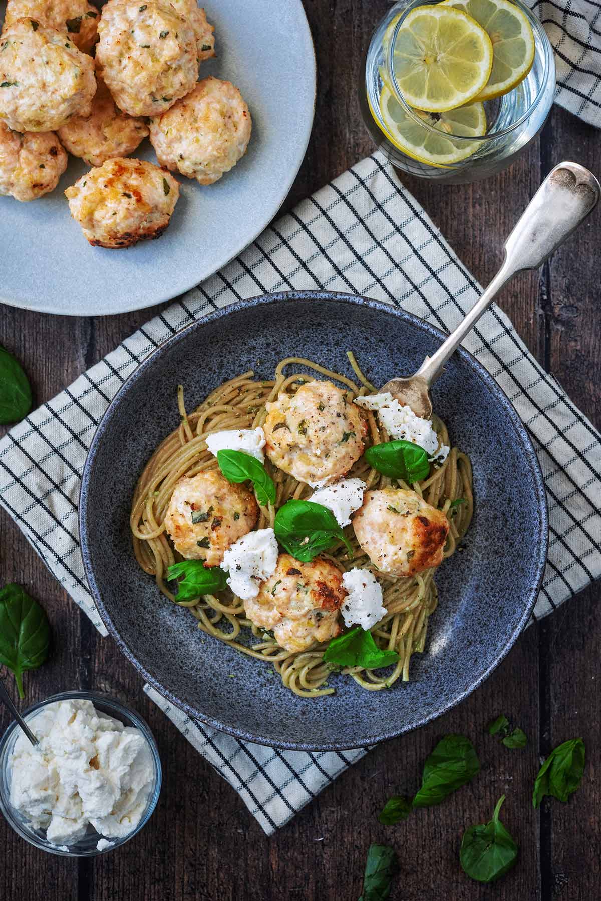 Chicken meatballs and spaghetti in a bowl next to a plate of more meatballs.