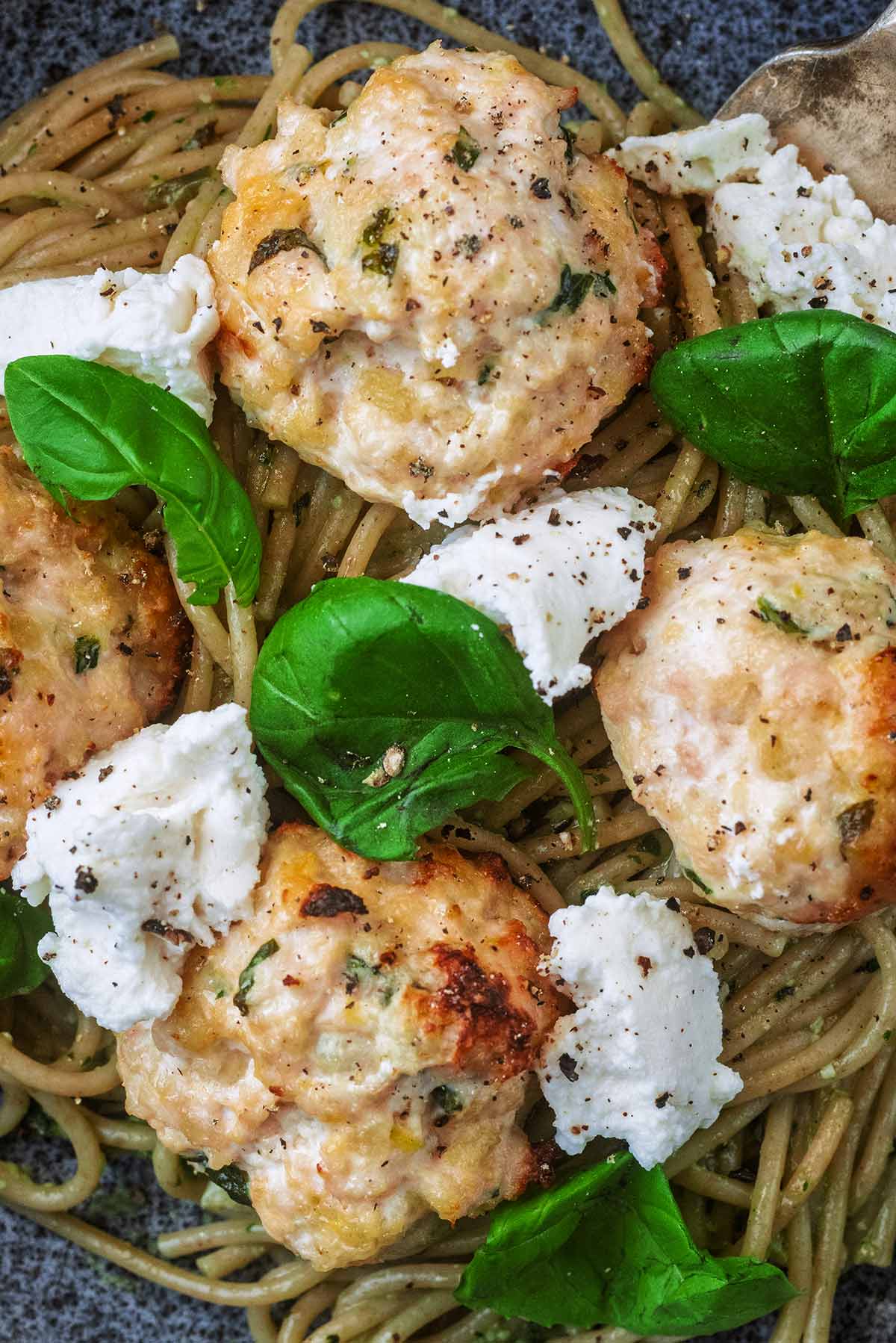 Four chicken meatballs on a bed of spaghetti with chunks of ricotta cheese and fresh basil leaves.