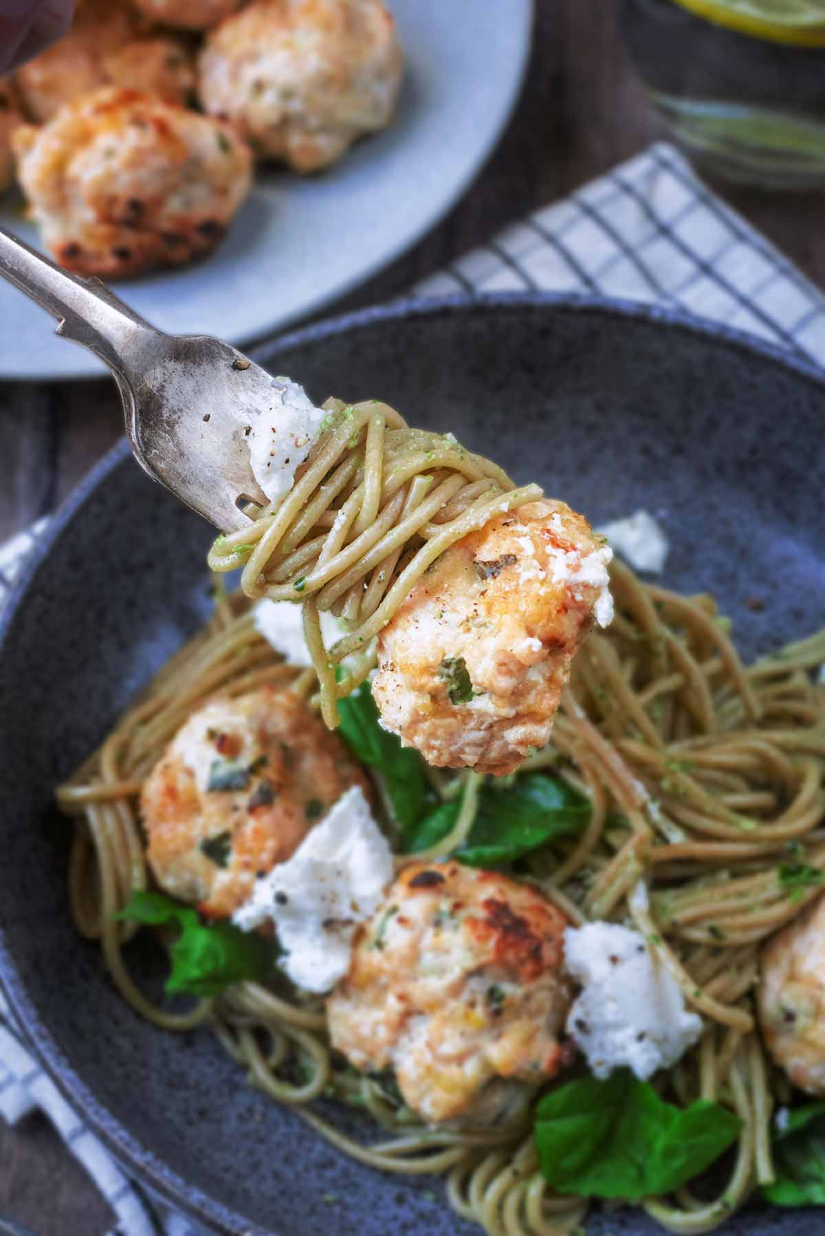 A fork lifting a meatball and some spaghetti from a bowl.