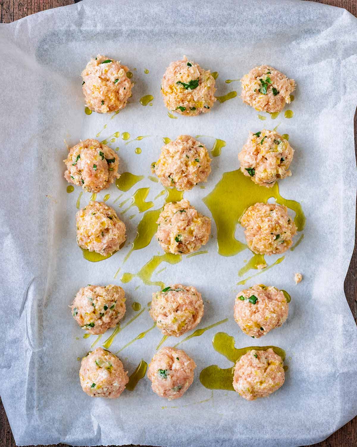 Fifteen uncooked chicken meatballs on a lined baking tray.