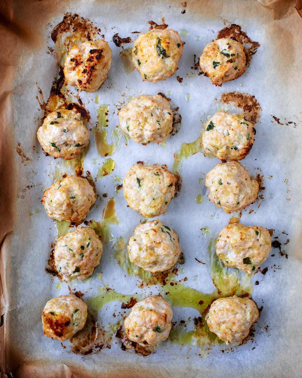 Fifteen cooked chicken meatballs on a baking tray.