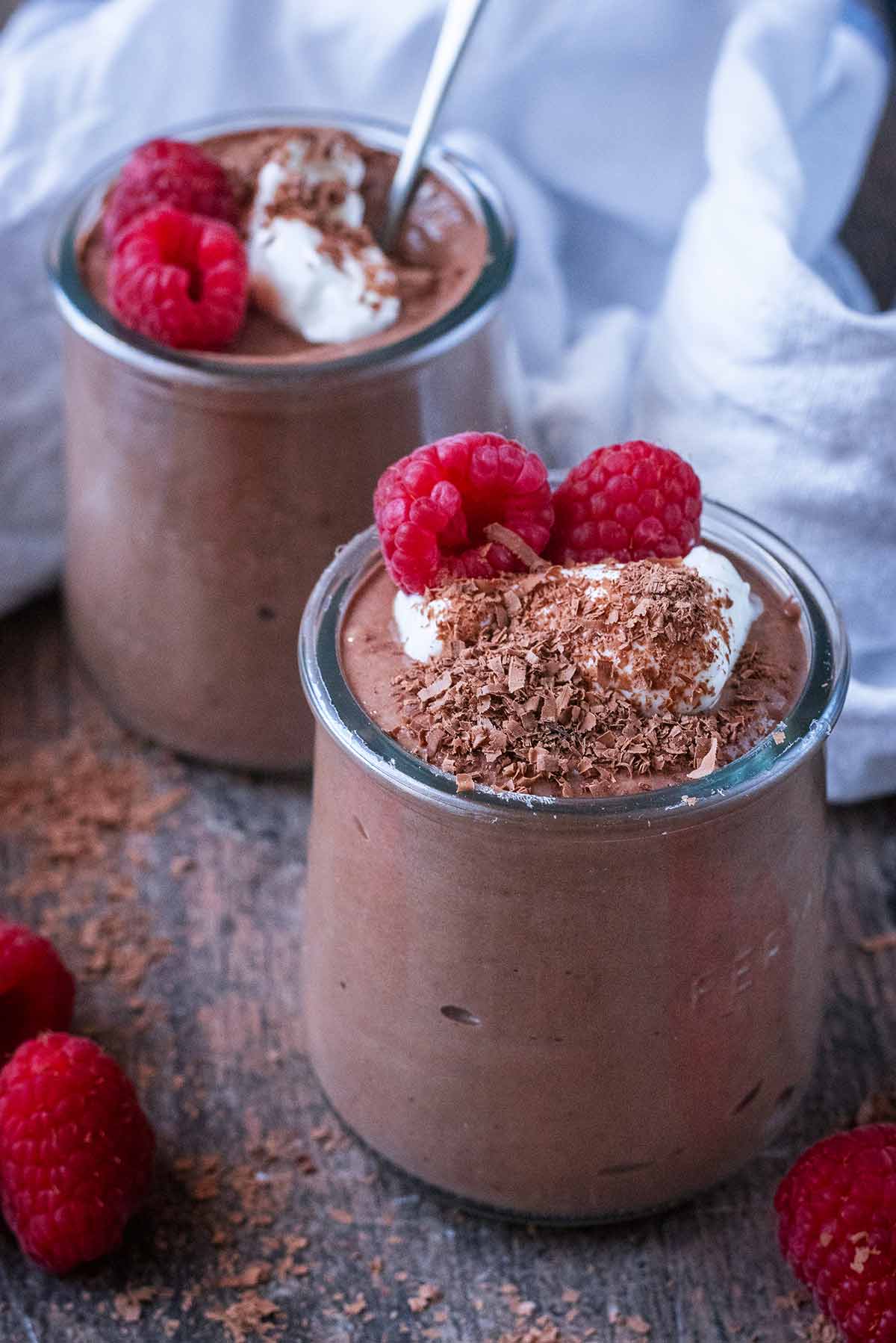 Two pots of chocolate pudding, one with a spoon in it.