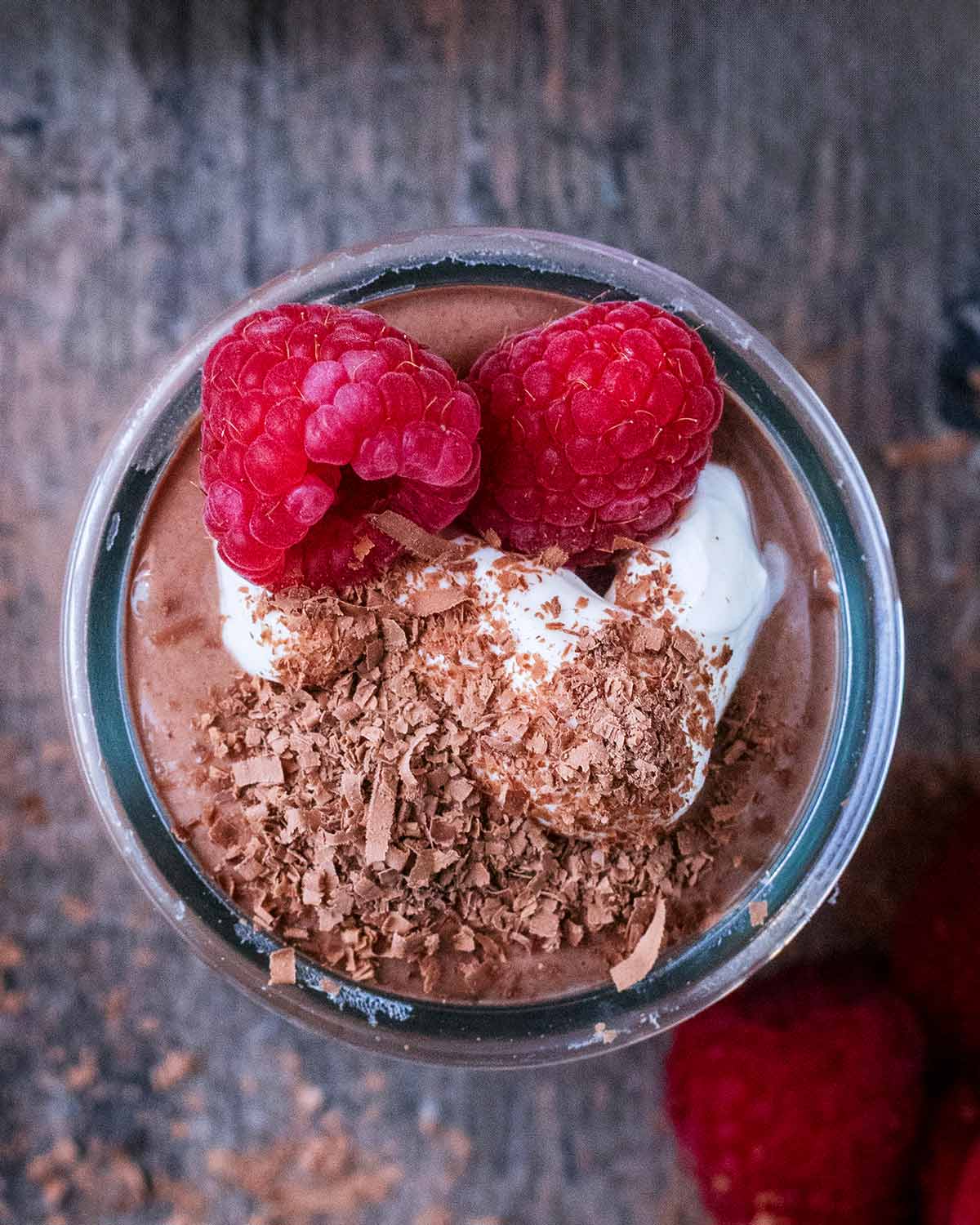 Chocolate pudding in a glass pot topped with yogurt, raspberries and grated chocolate.