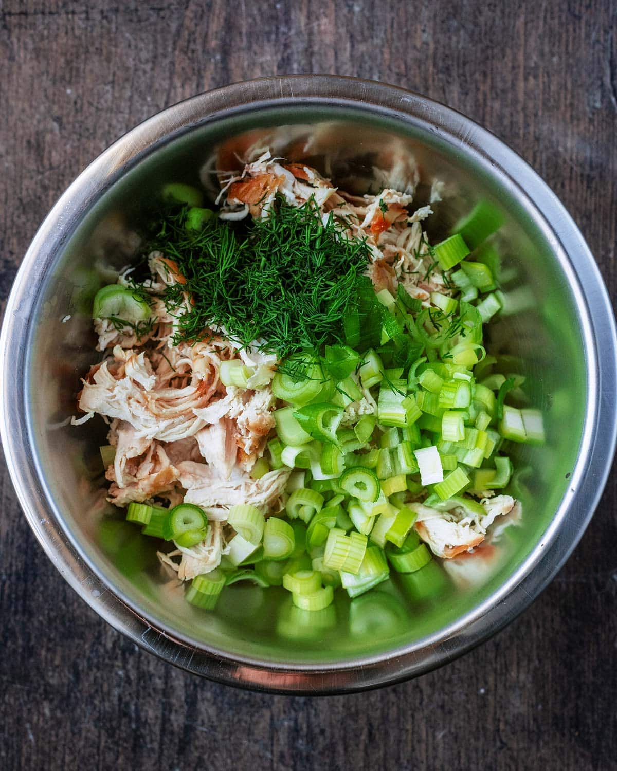 Shredded cooked chicken, green onions and chopped dill in a mixing bowl.