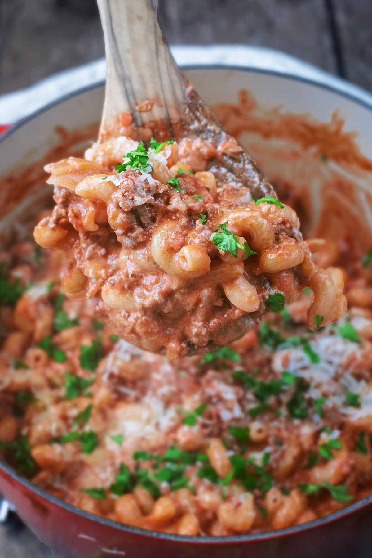 A wooden spoon lifting some beef pasta out of a large cooking pan.