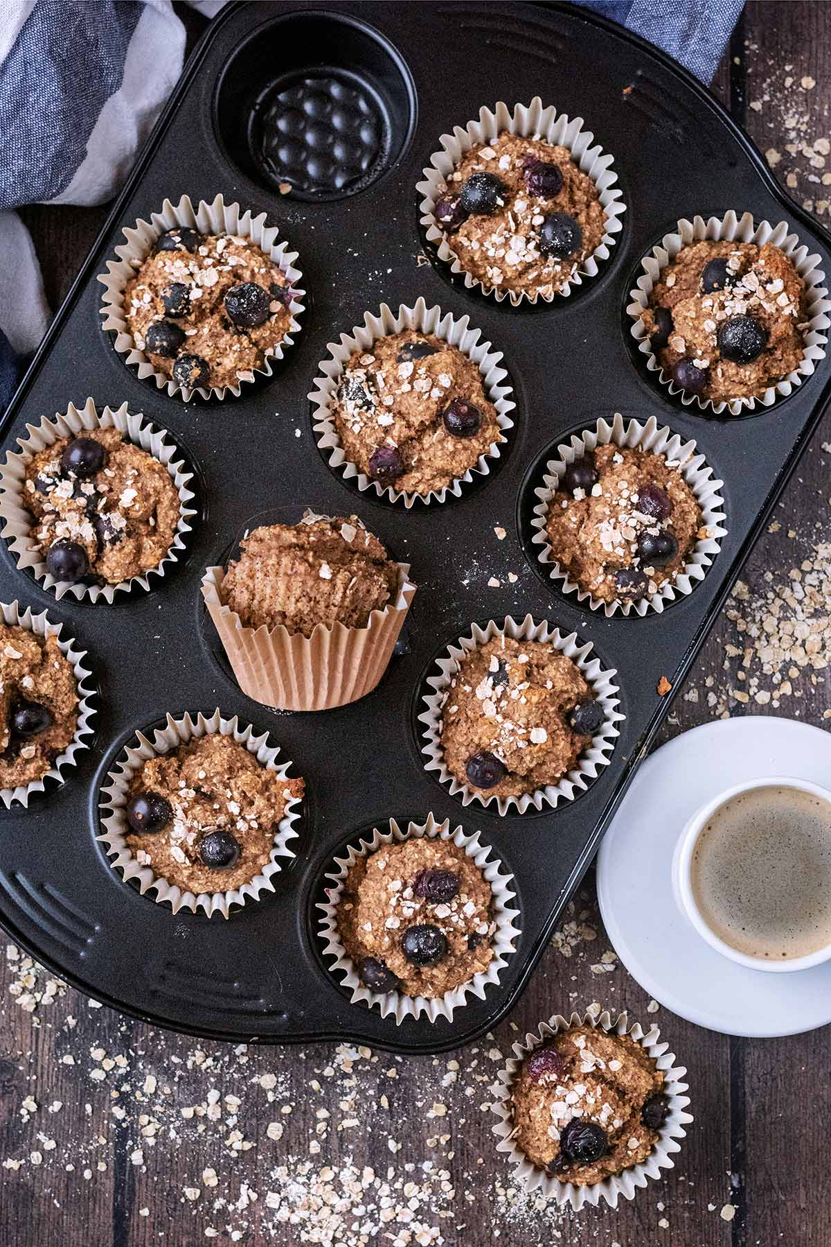 Blueberry muffins in a muffin tin on a wooden surface.