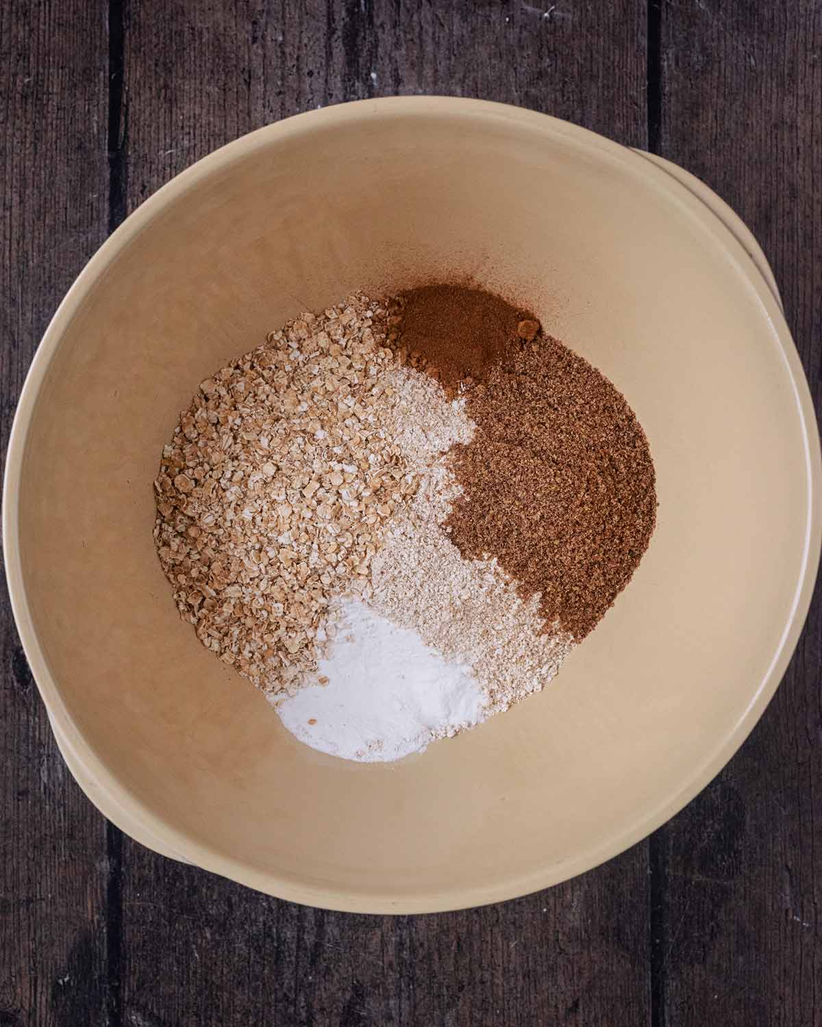 A mixing bowl containing oat flour, whole oats, spices and baking powder.