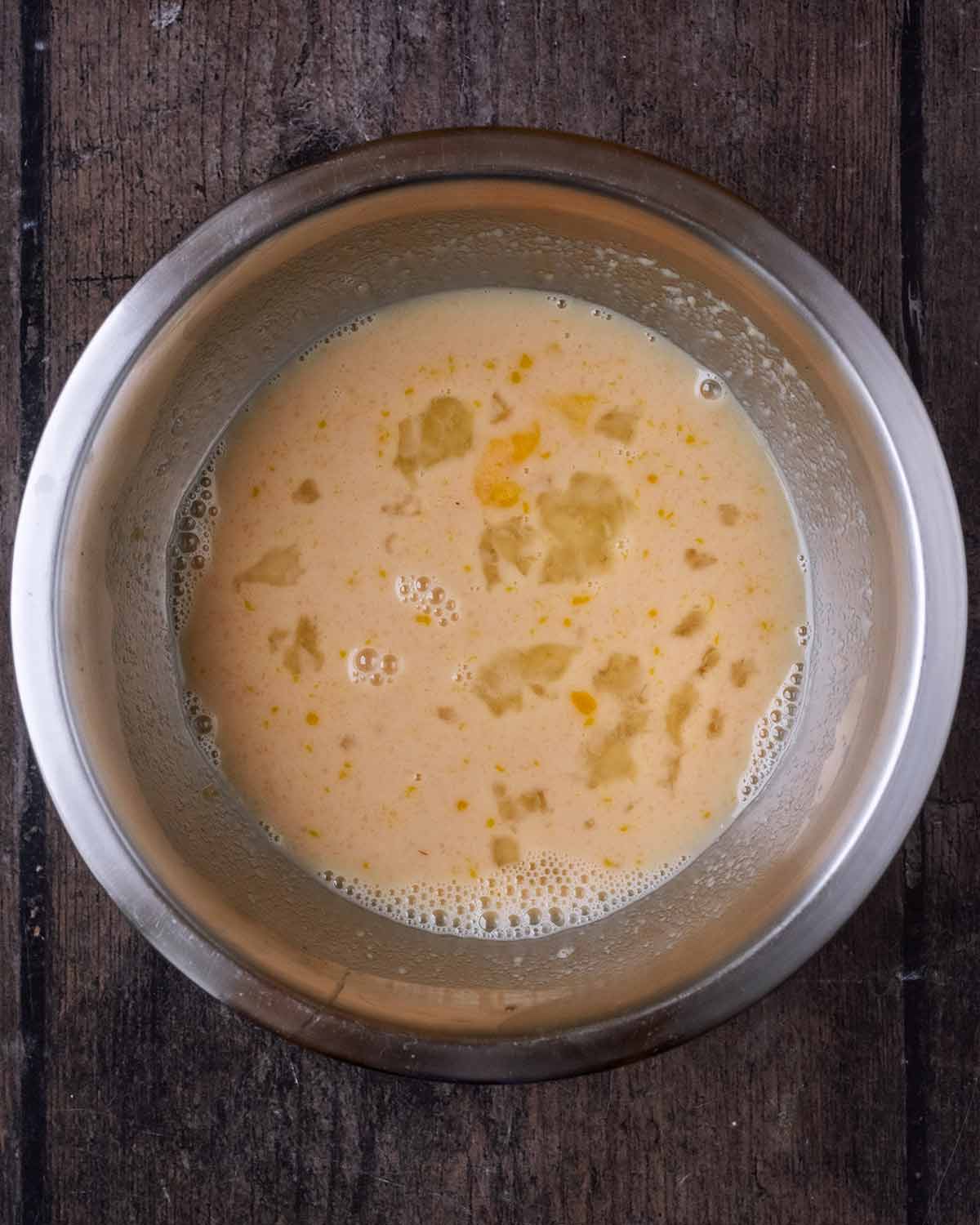 A metal mixing bowl containing milk, egg, vanilla, apple sauce and maple syrup.