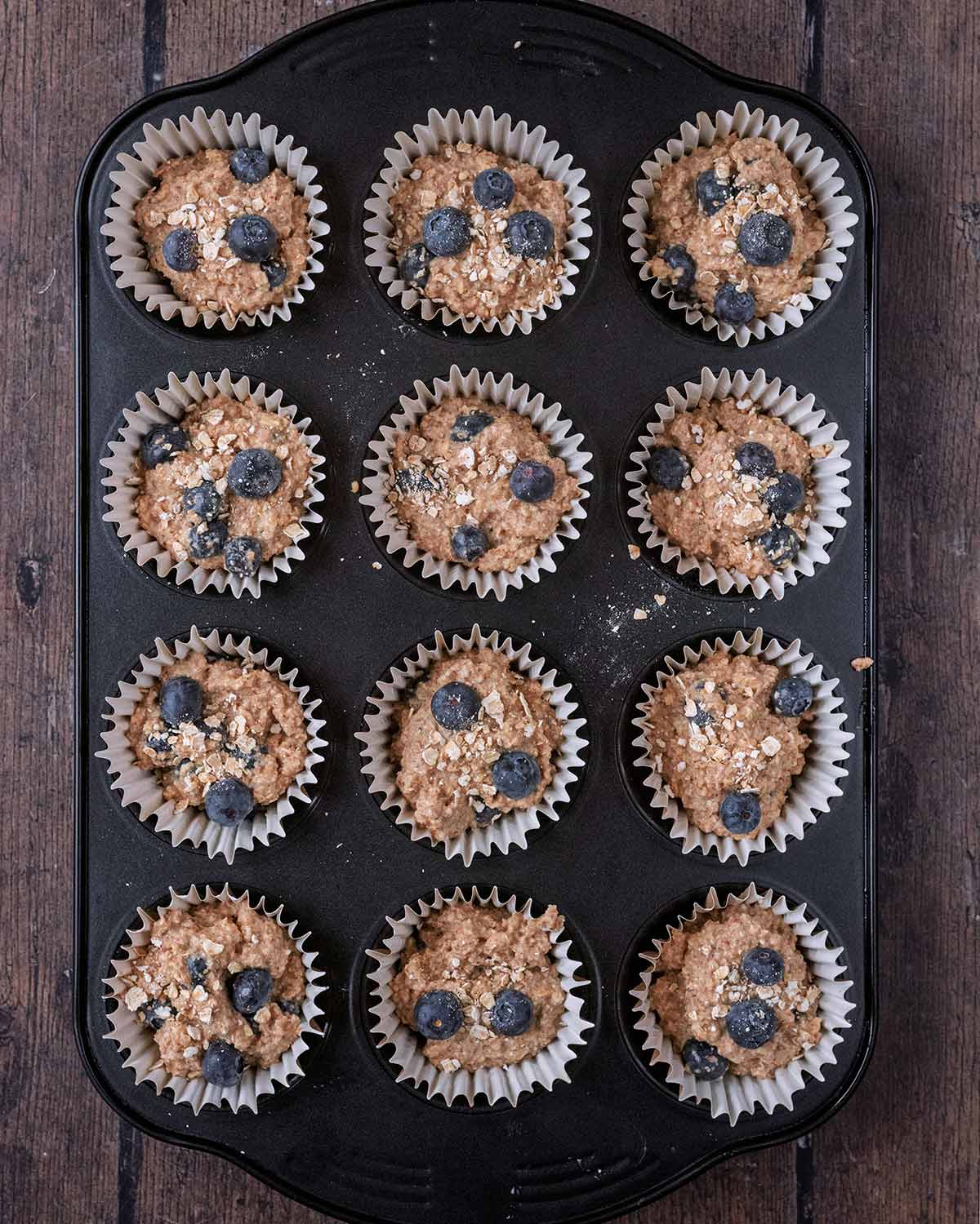 Twelve hole muffin tin with muffin batter in cases.