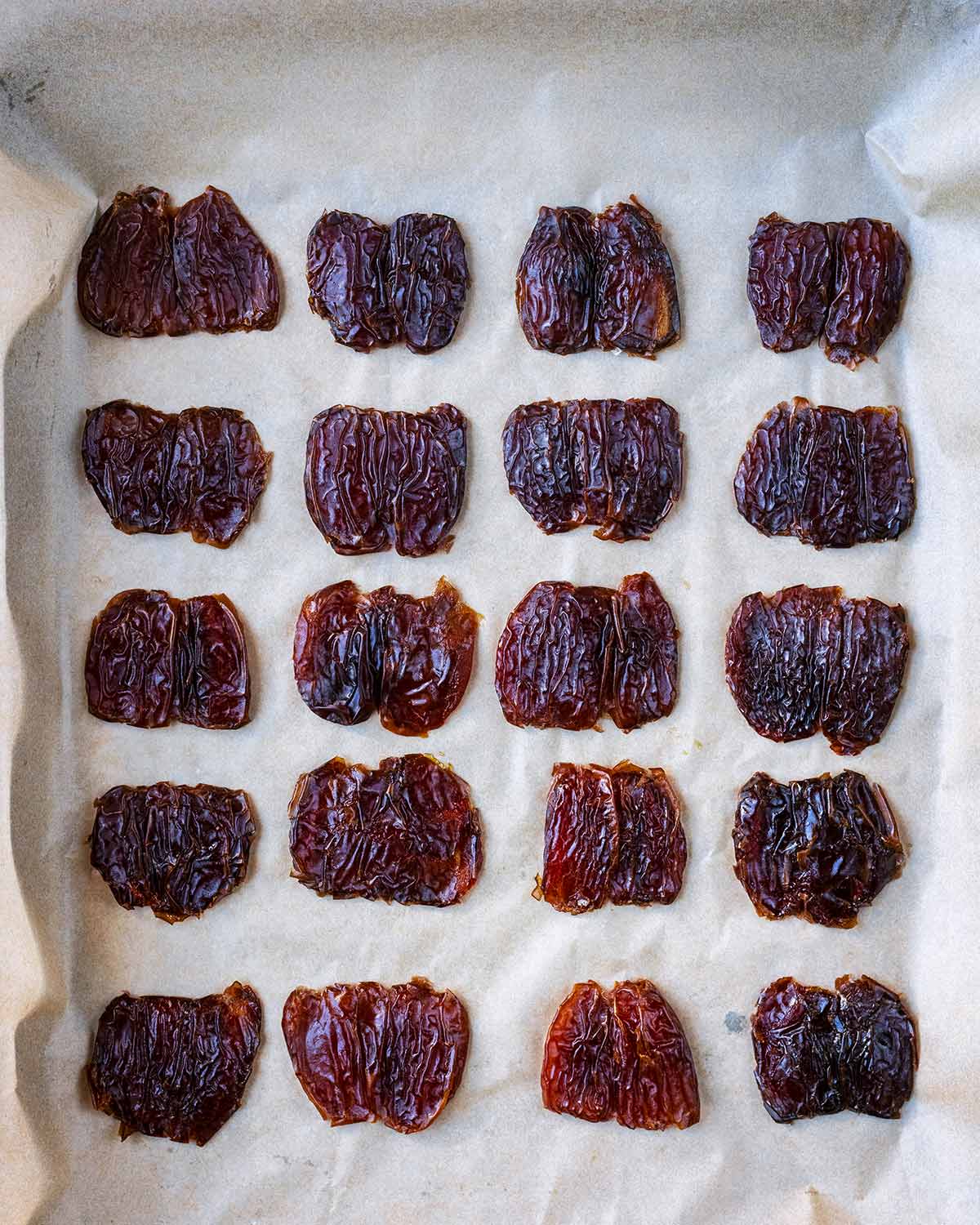 Twenty Medjool dates, de-stoned and flattened on a lined baking sheet.