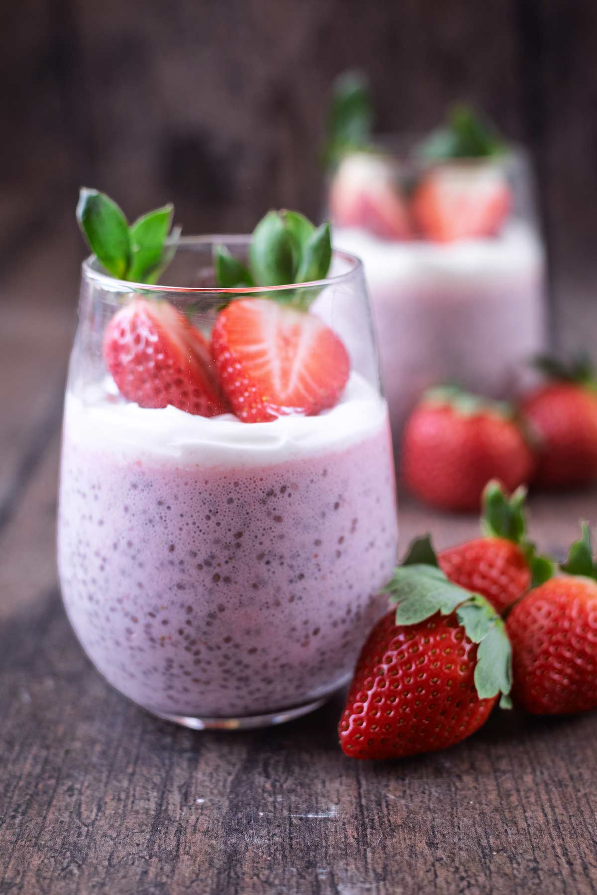 A serving glass containing strawberry pudding with another glass of pudding in the background.