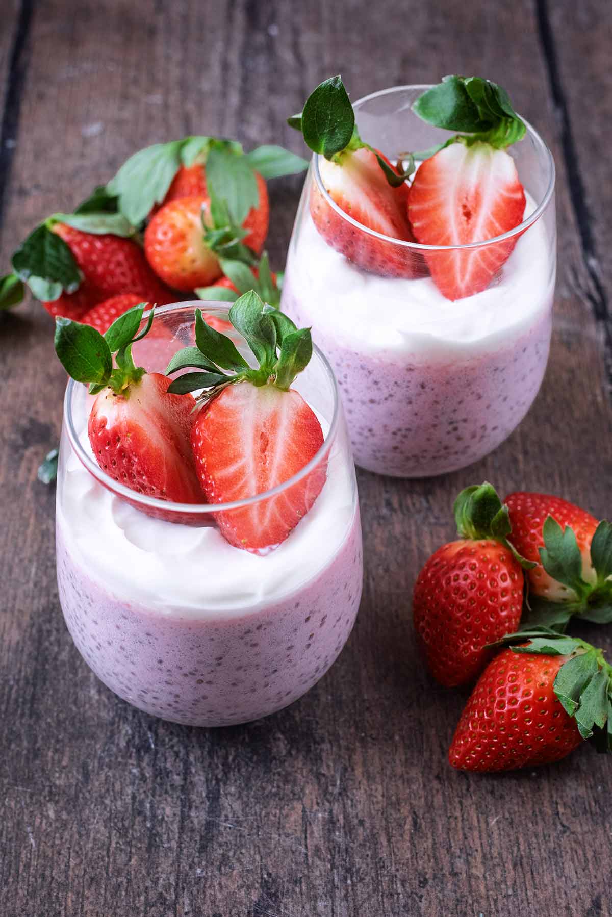 Two glasses of strawberry pudding, topped with fresh strawberries, on. wooden surface.