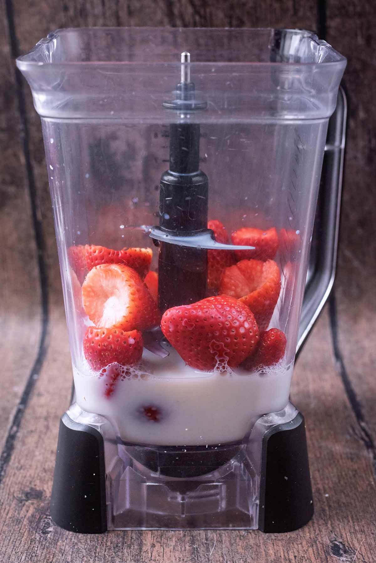 Milk and strawberries in a large blender jug.