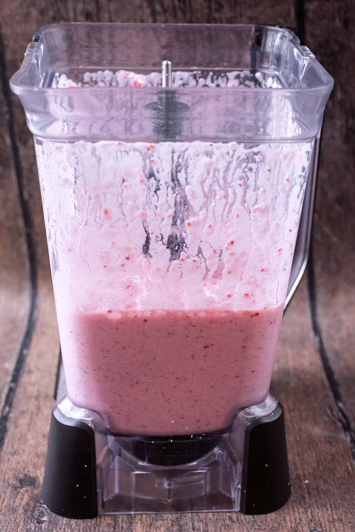 Milk and strawberries blended together in a blender jug.