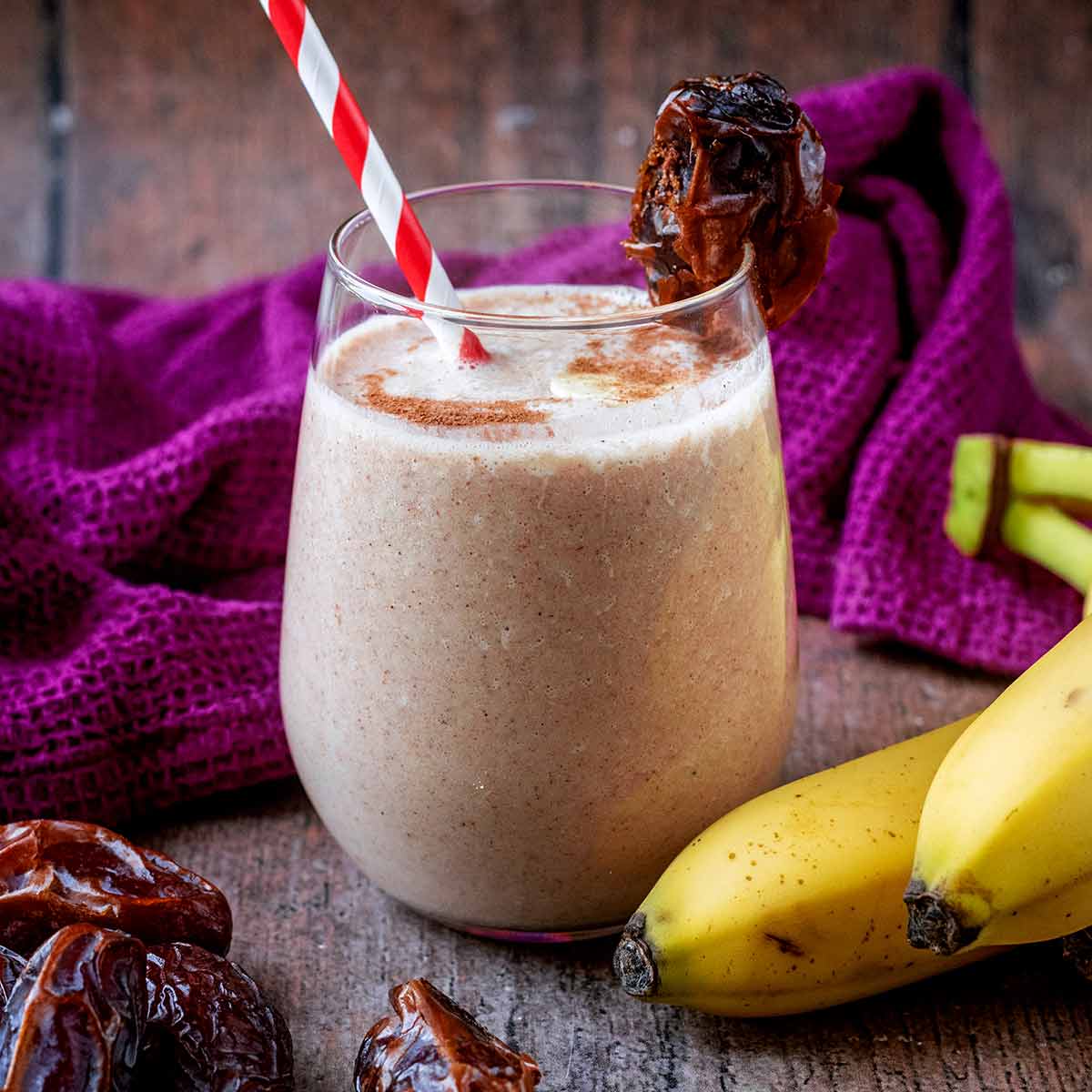 A glass of banana date smoothie in front of a purple towel.
