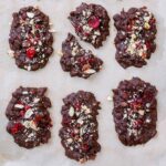 Six homemade fruit and nut chocolate bars on a lined baking tray.