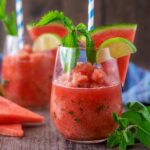 A glass of watermelon slushie with slices of watermelon and lime on the rim.