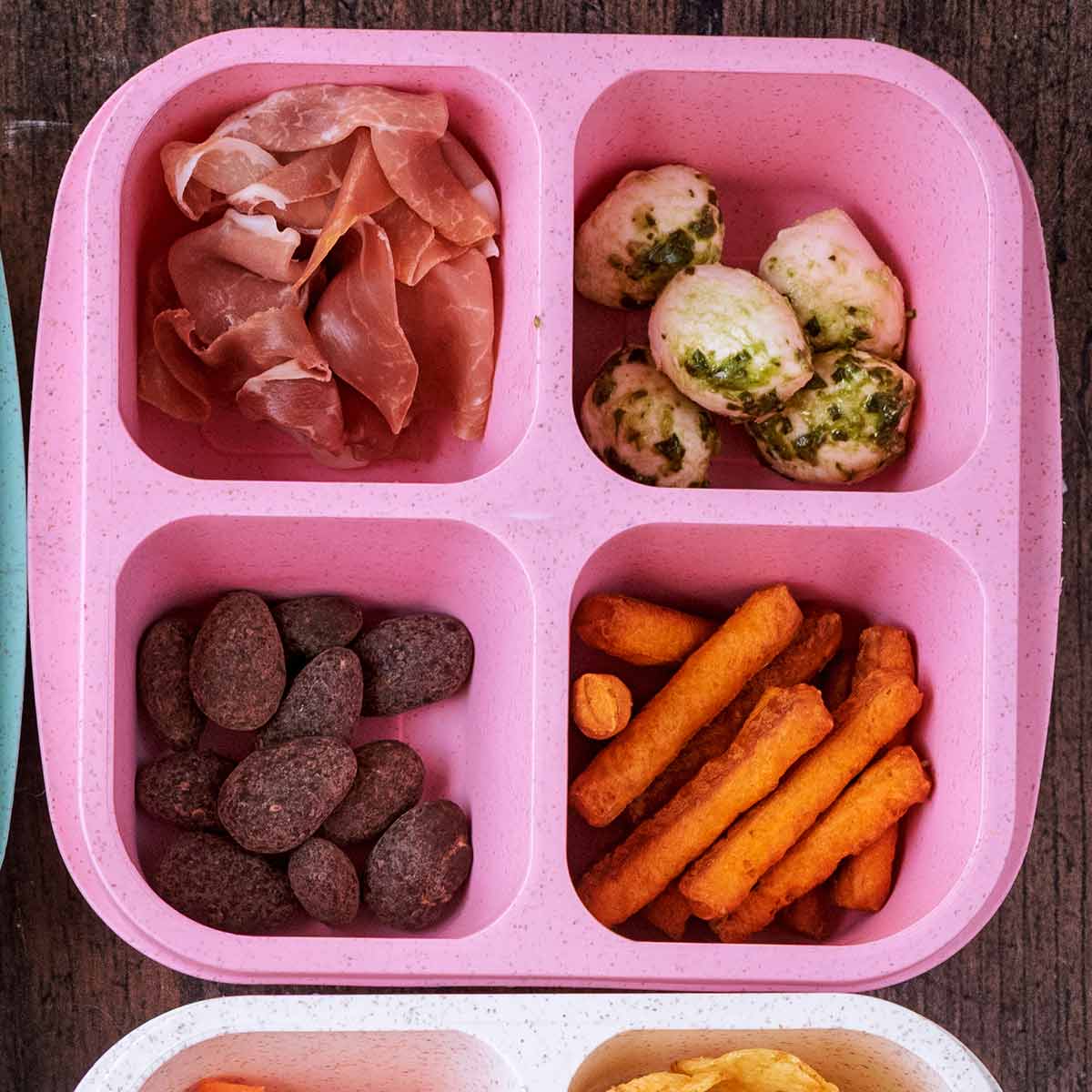 A four compartment snack box containing ham, mozzarella, breadsticks and almonds.