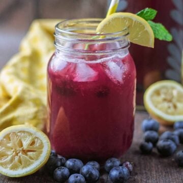 Blueberry lemonade in a mason jar next to lemon halves and blueberries.
