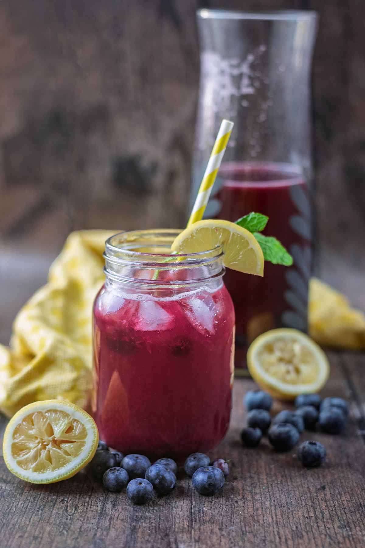 A glass of purple coloured drink with a carafe of more drink in the background.