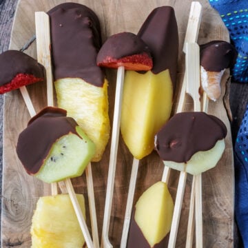 Chocolate dipped fruit skewers on a wooden surface.