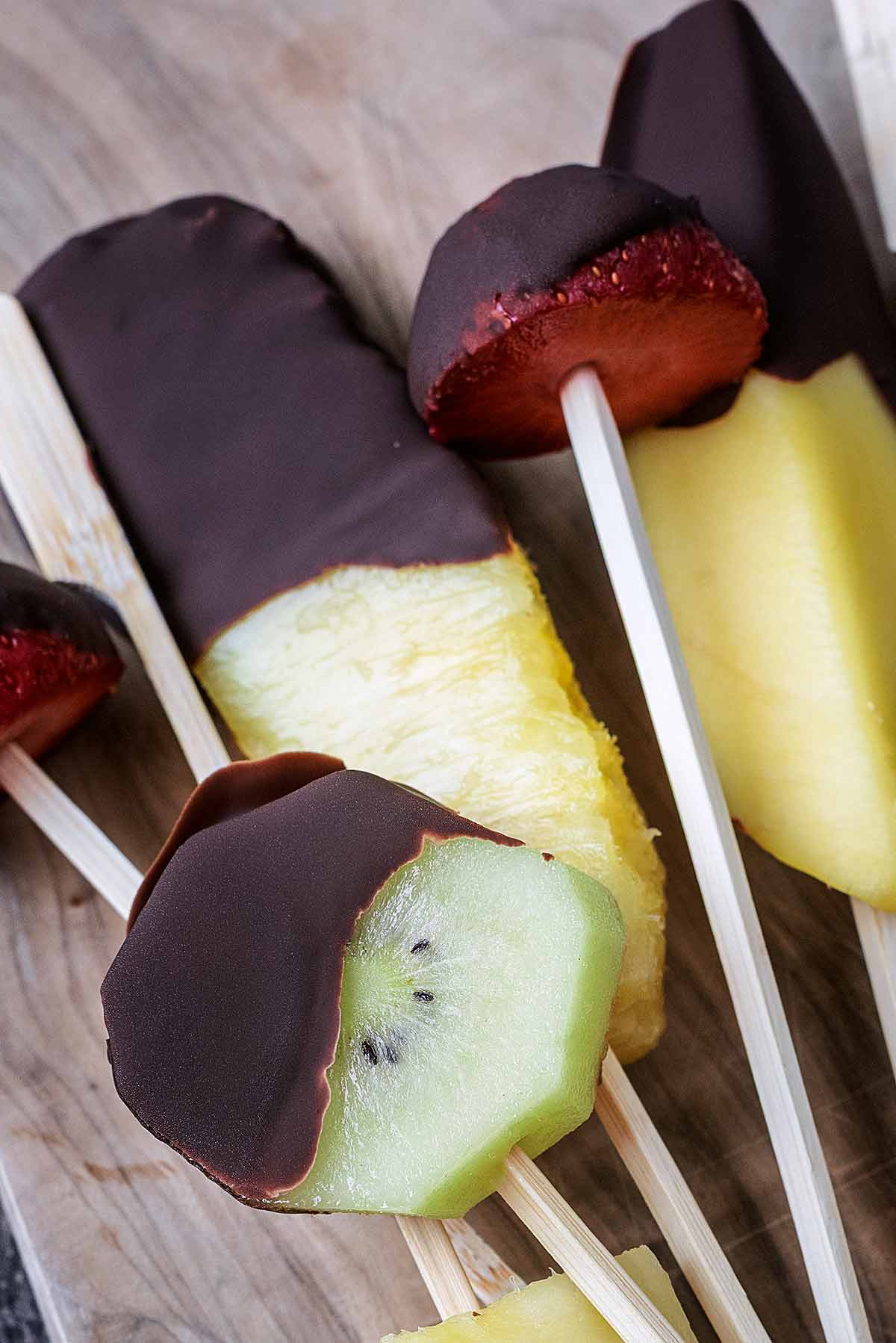 Various chocolate covered fruit on wooden skewers.