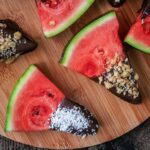 Two slices of chocolate dipped watermelon on a wooden board.