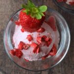 Ninja Creami strawberry ice cream topped with small strawberry pieces and a whole strawberry.