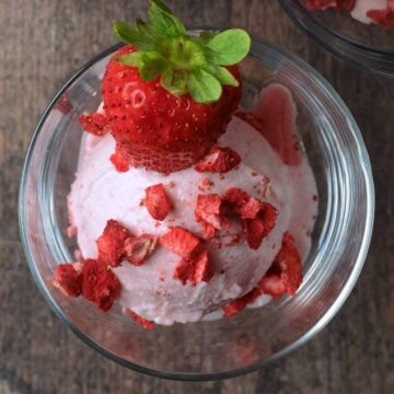 Ninja Creami strawberry ice cream topped with small strawberry pieces and a whole strawberry.