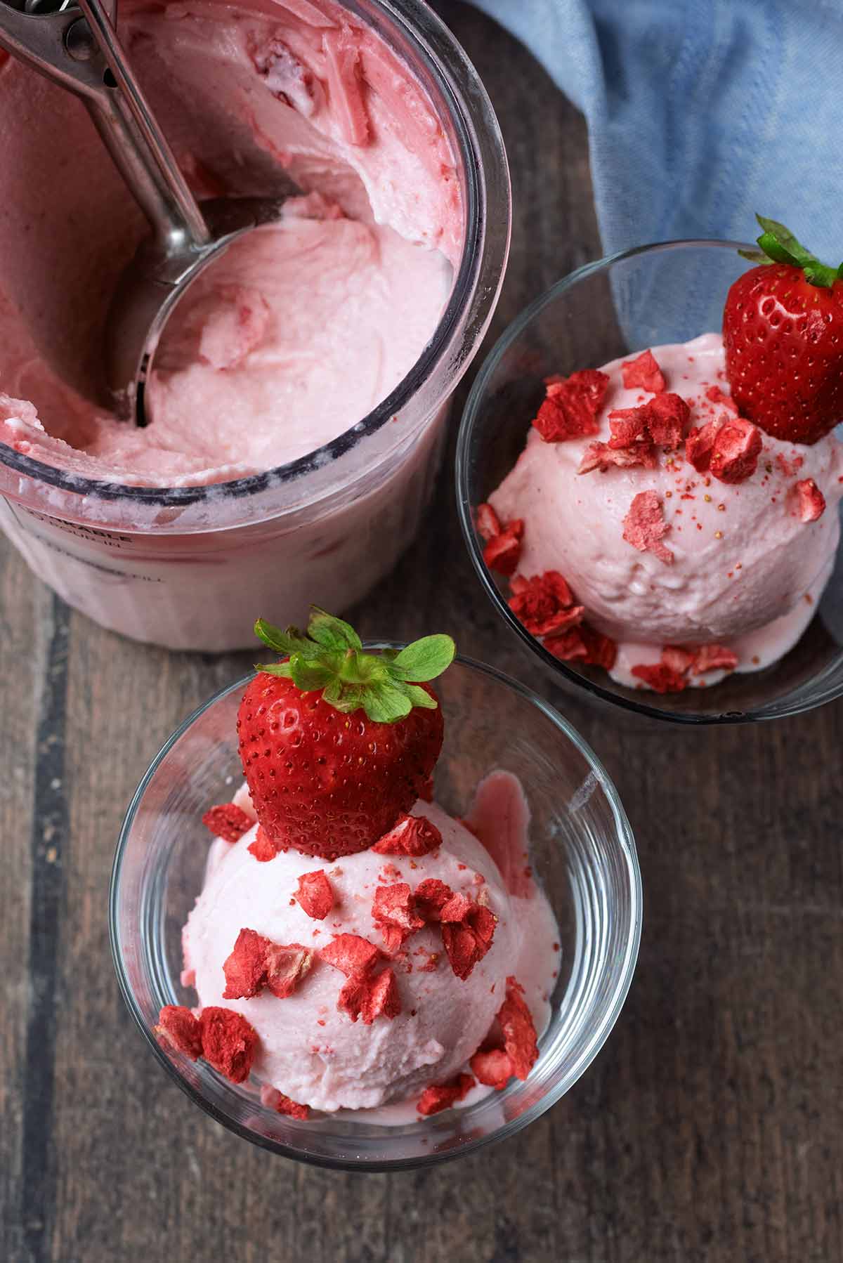 Two serving glasses of strawberry ice cream next to a tub of more ice cream.