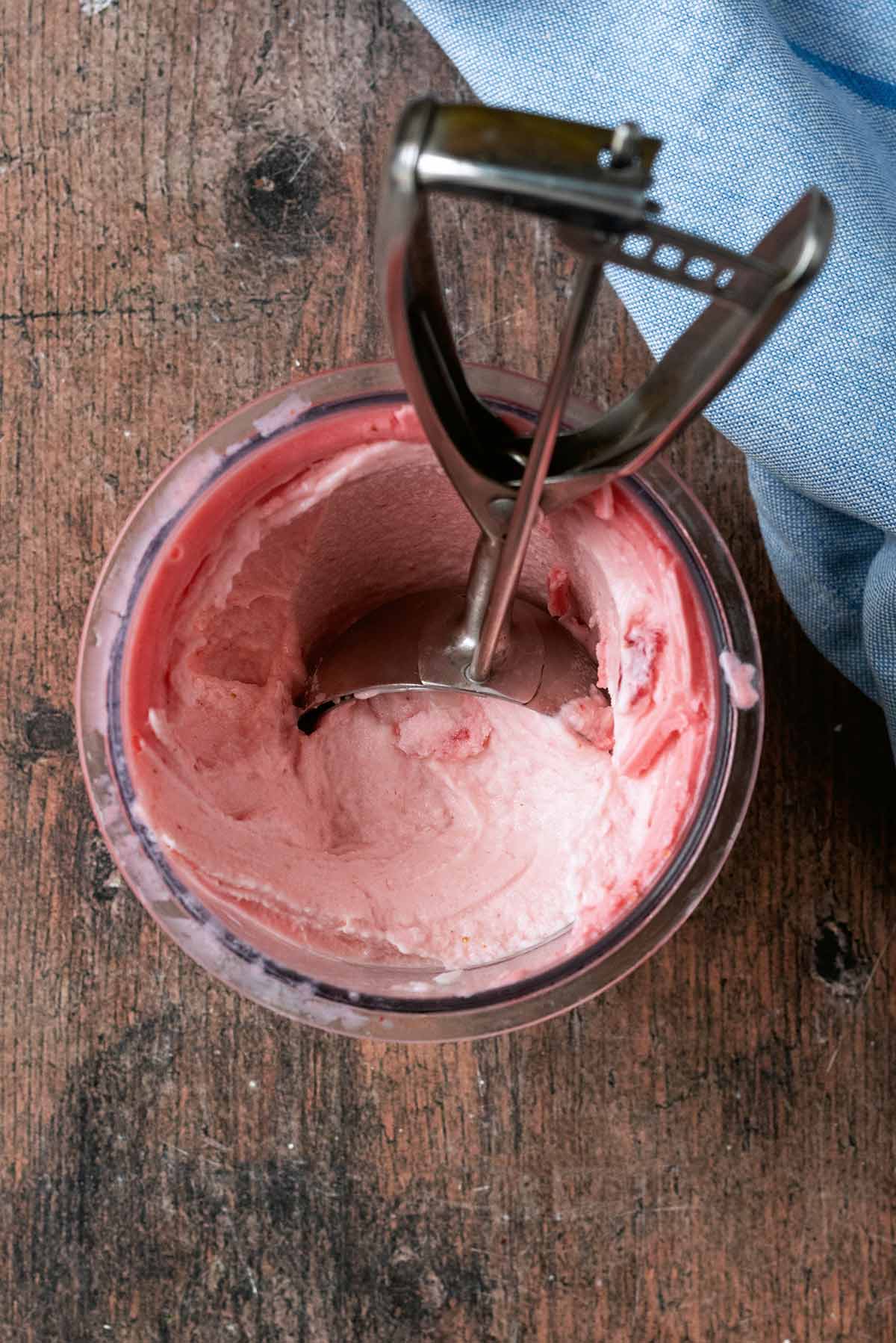 A Ninja Creami pint container full of strawberry ice cream and an ice cream scoop.