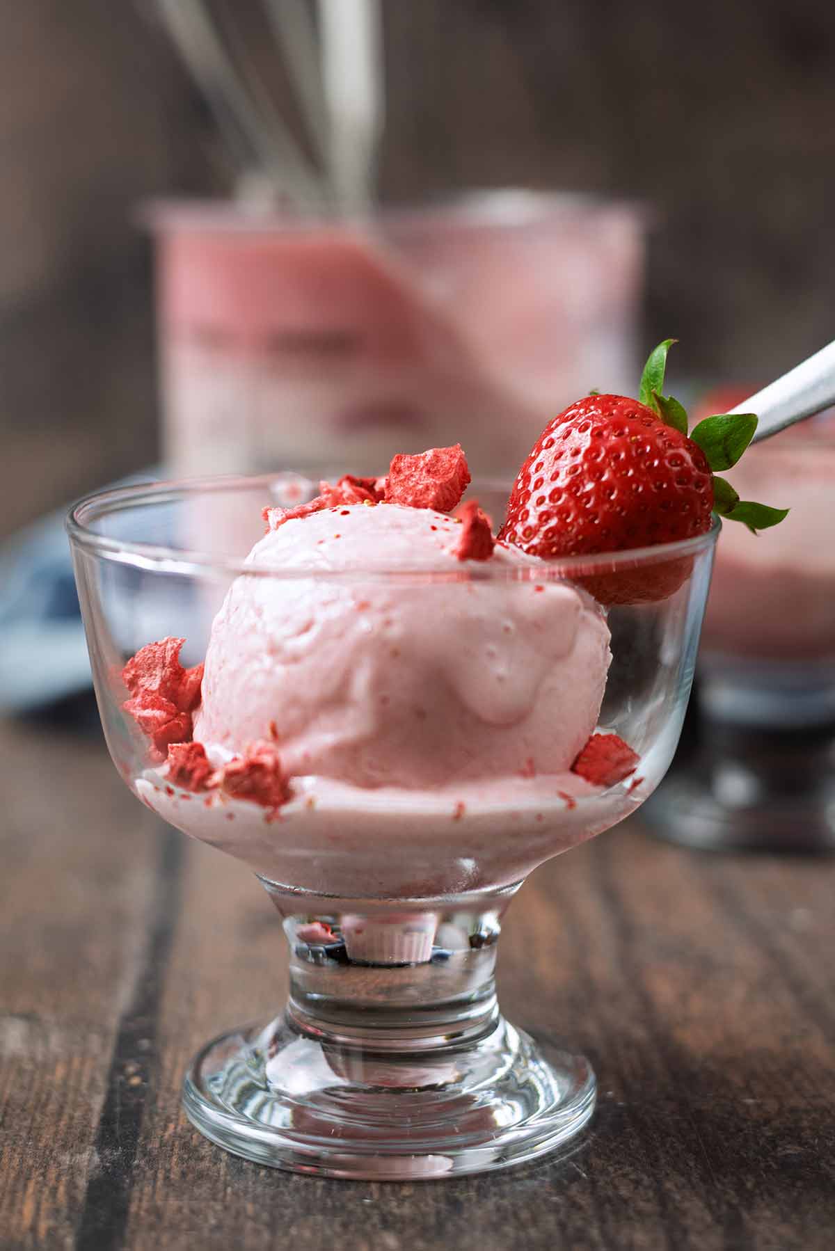 A serving glass of strawberry ice cream topped with a whole strawberry and some strawberry pieces.