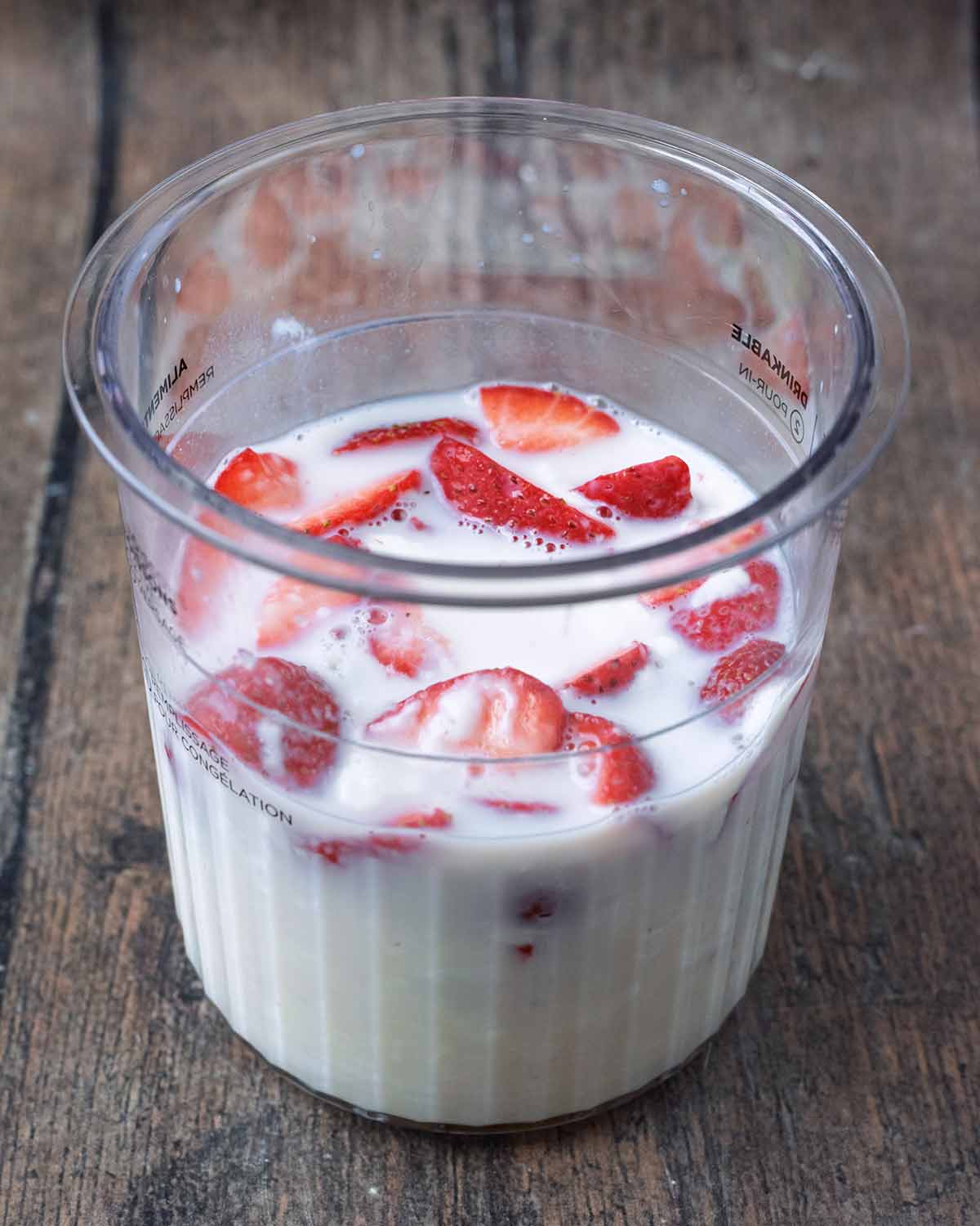 A Ninja Creami tub containing yogurt, milk and strawberries.