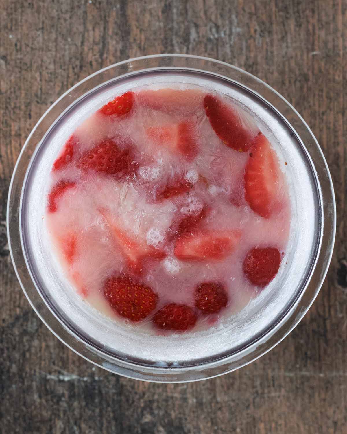 A frozen pint tub of yogurt, milk and strawberries.