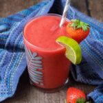 A glass full of strawberry watermelon smoothie next to a blue towel.