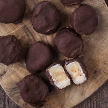 Chocolate dipped frozen yogurt banana slices on a wooden surface.