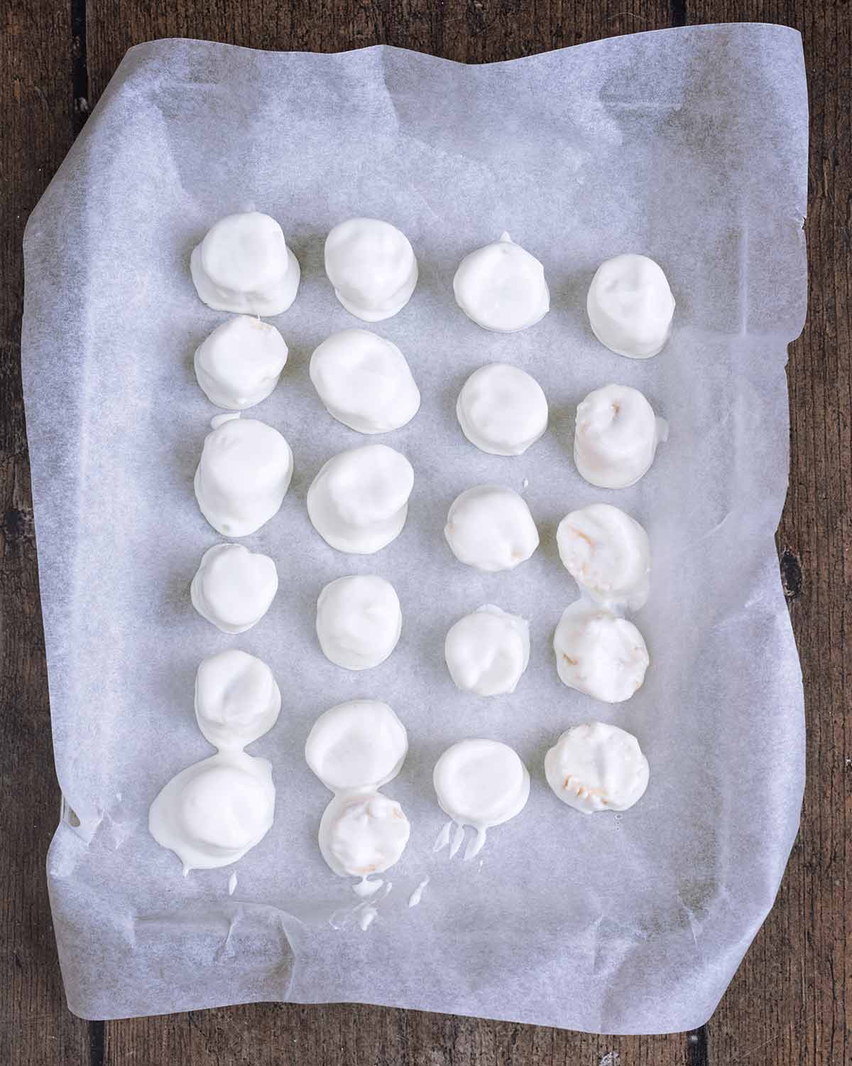 Frozen yogurt covered banana slices on a lined baking sheet.