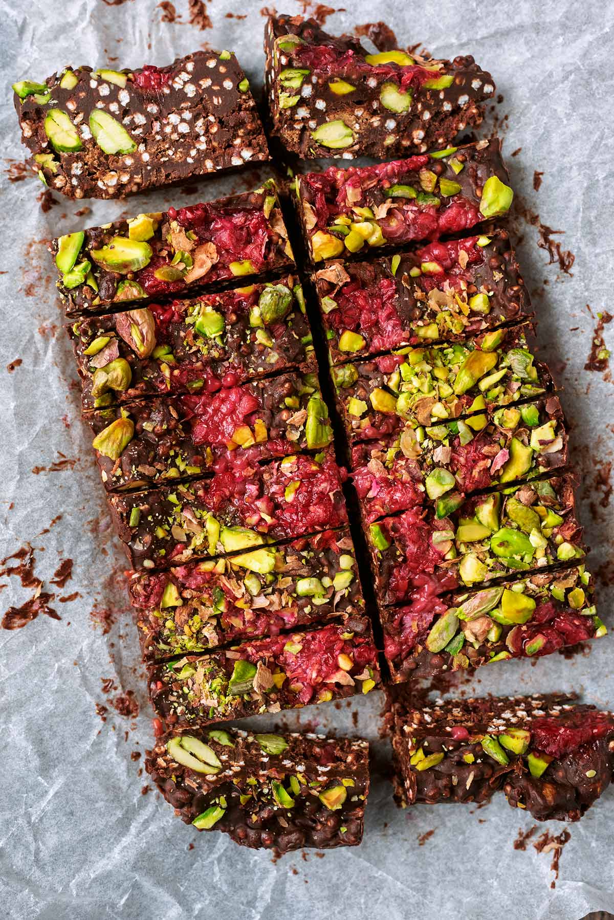 A slab of chocolate topped with pistachios and raspberries, cut into 16 bars.
