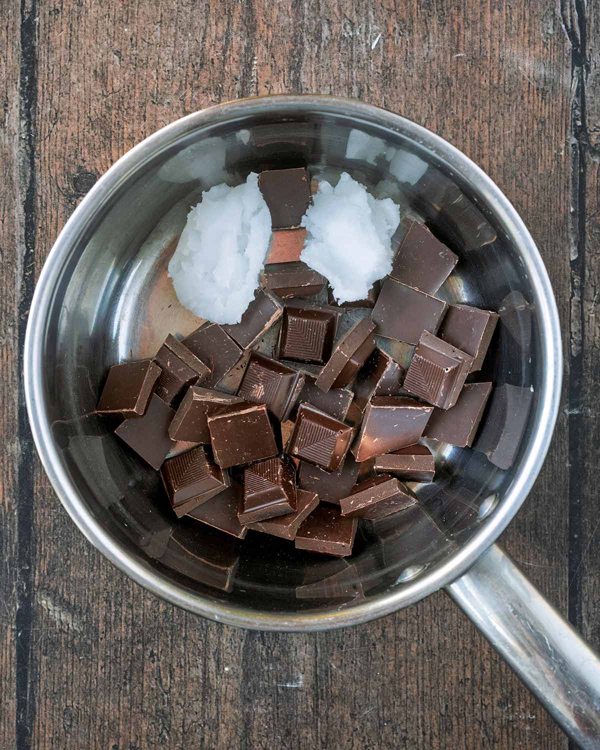 Chunks of dark chocolate and some coconut oil in a silver saucepan.