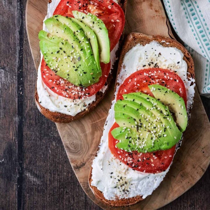 Two slices of avocado cream cheese toast on a wooden board.