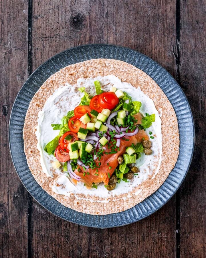 A wrap covered in cream cheese then topped with smoked salmon and salad items.