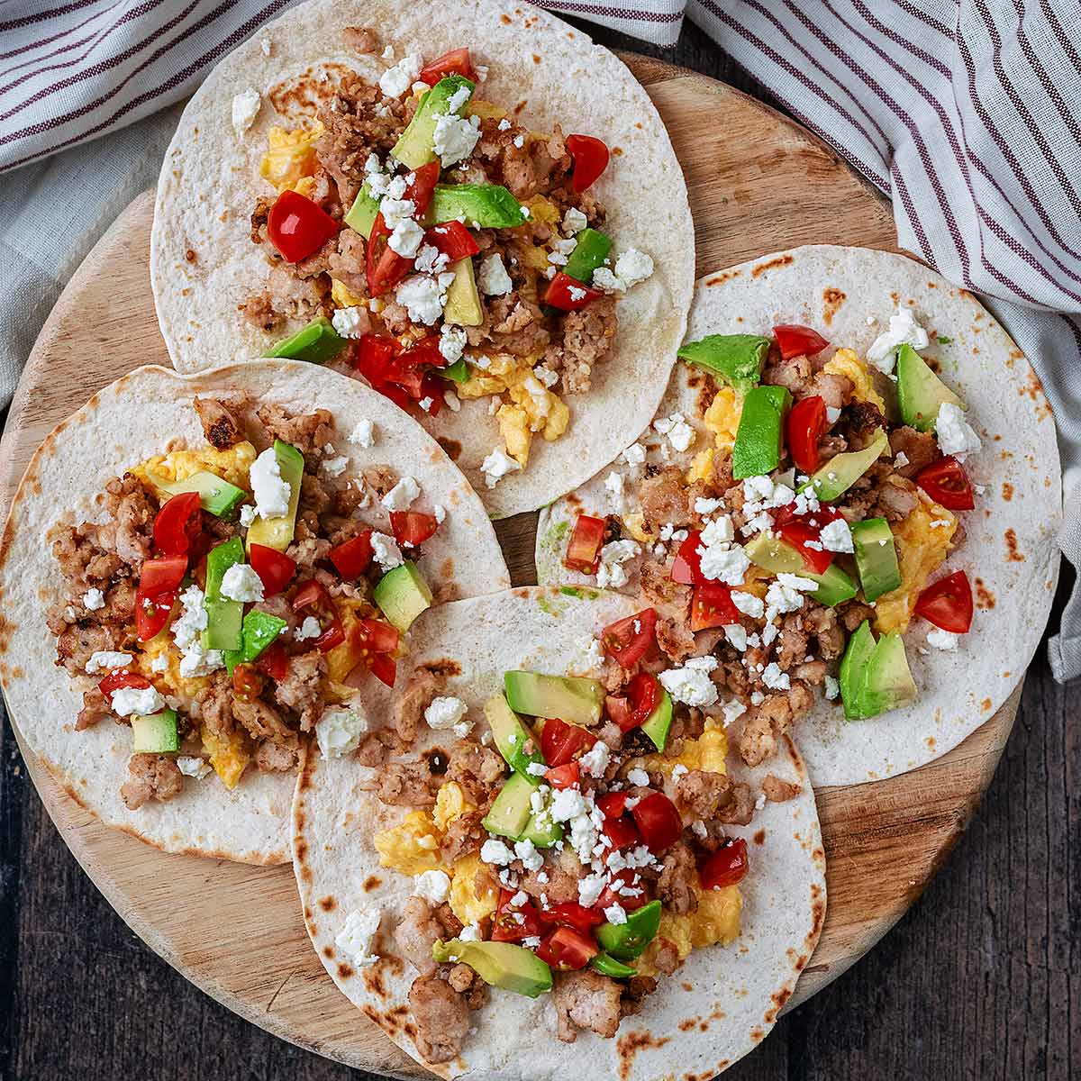 Four breakfast tacos on a round wooden board.