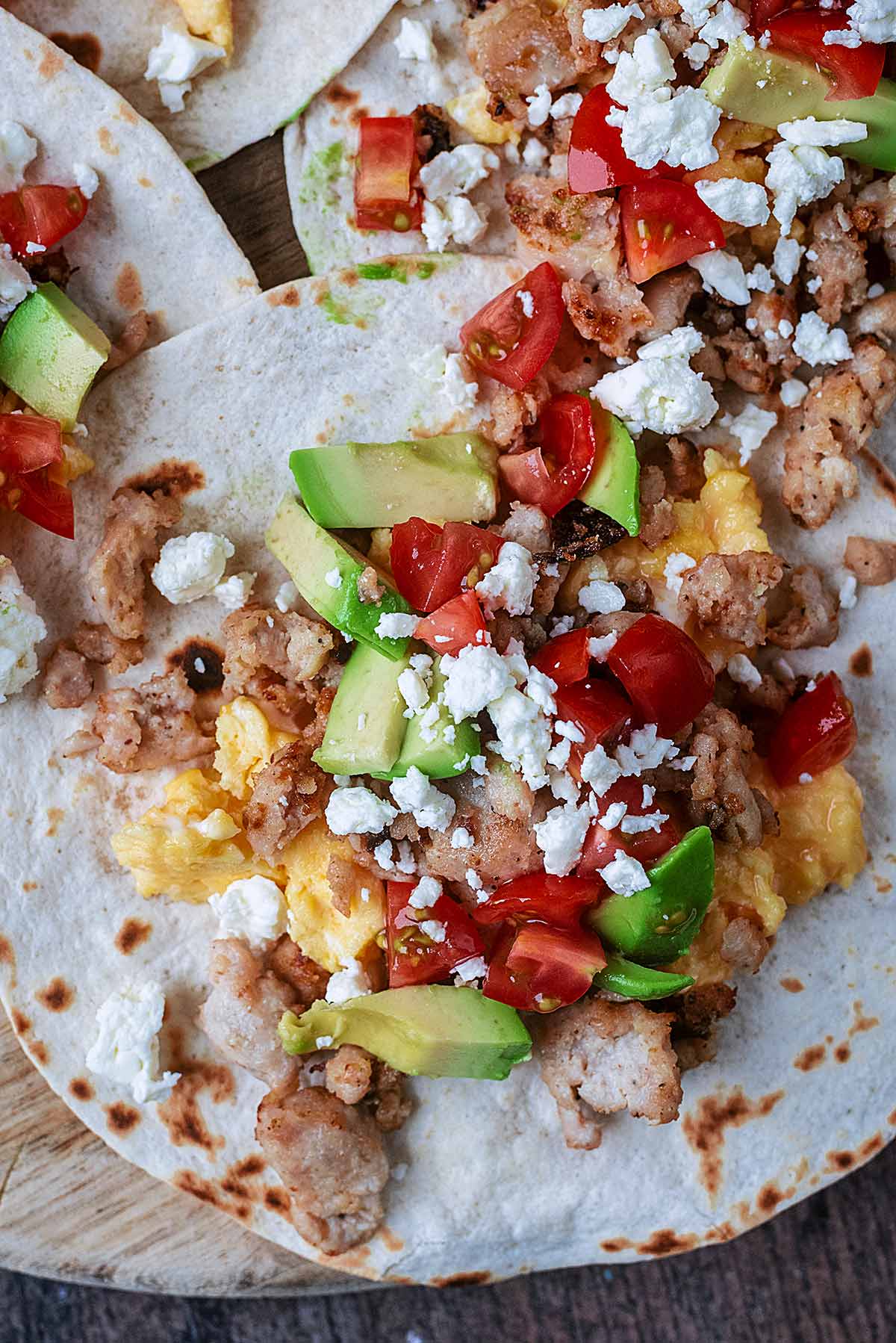 A sausage and egg taco topped with diced tomato, avocado and feta.