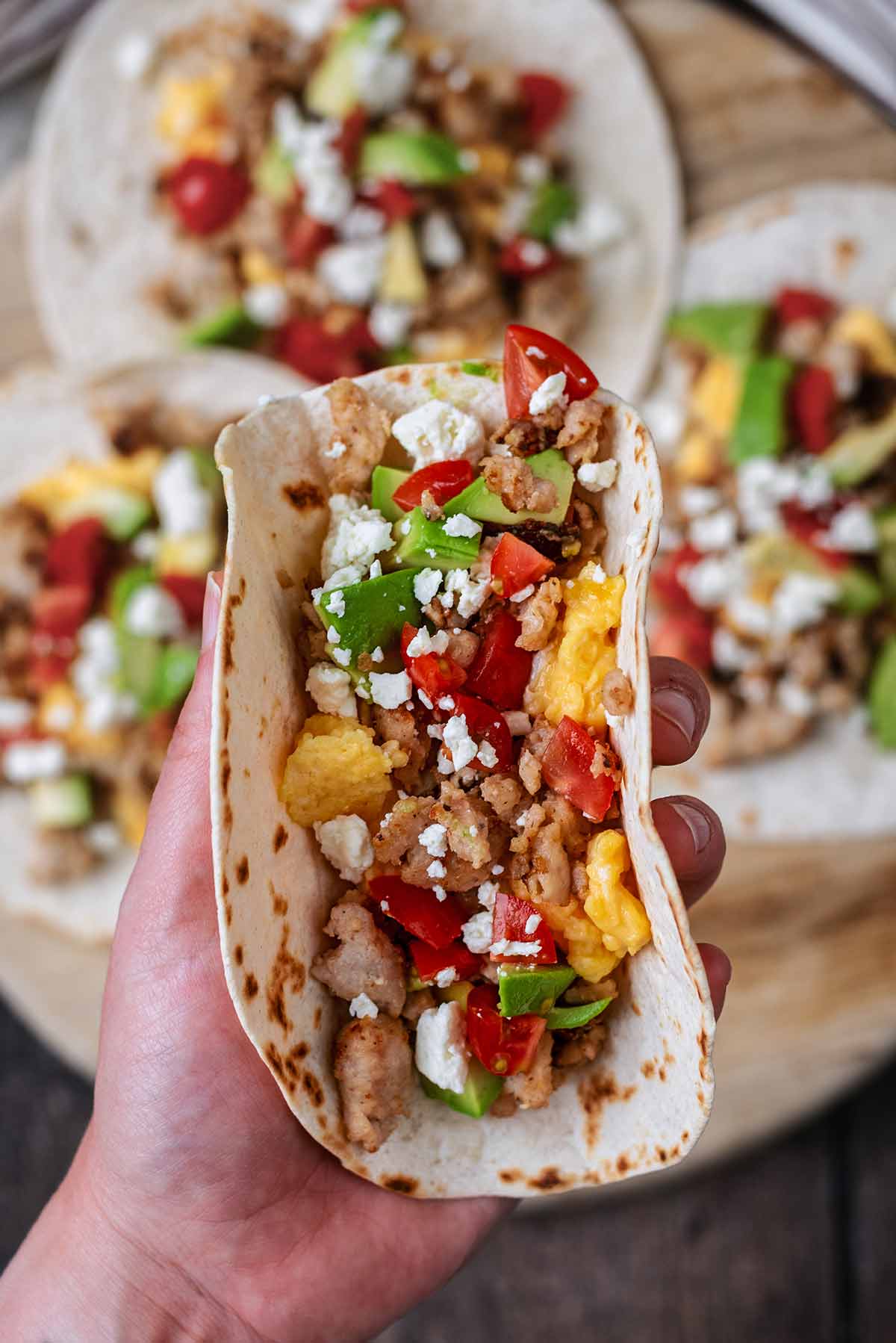 A hand holding a breakfast taco above three other tacos.