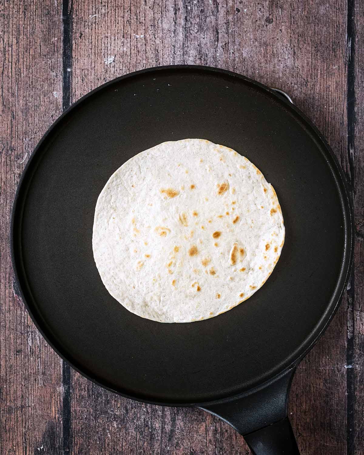 A small flour tortilla heating on a flat pan.