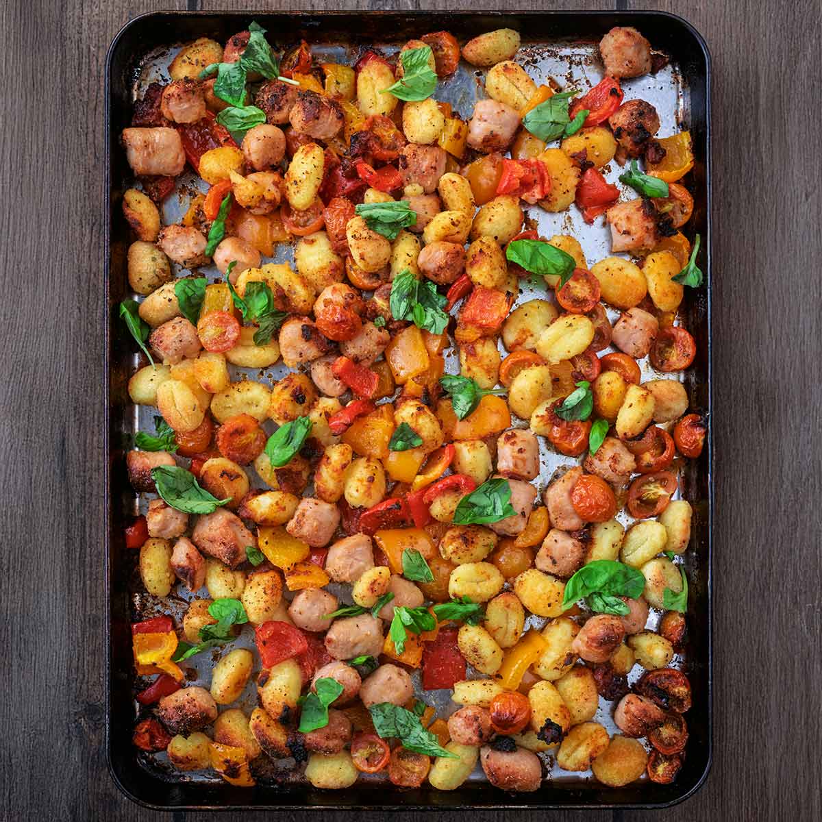 Chicken sausage tray bake on a wooden surface.